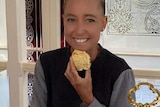 A young woman with a big smile, holding a scone at a high tea.