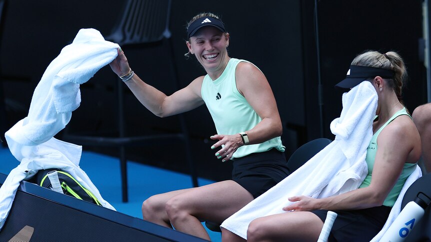Caroline Wozniacki laughs with Angelique Kerber, who is covering her face with a towel, at an Australian Open practice.