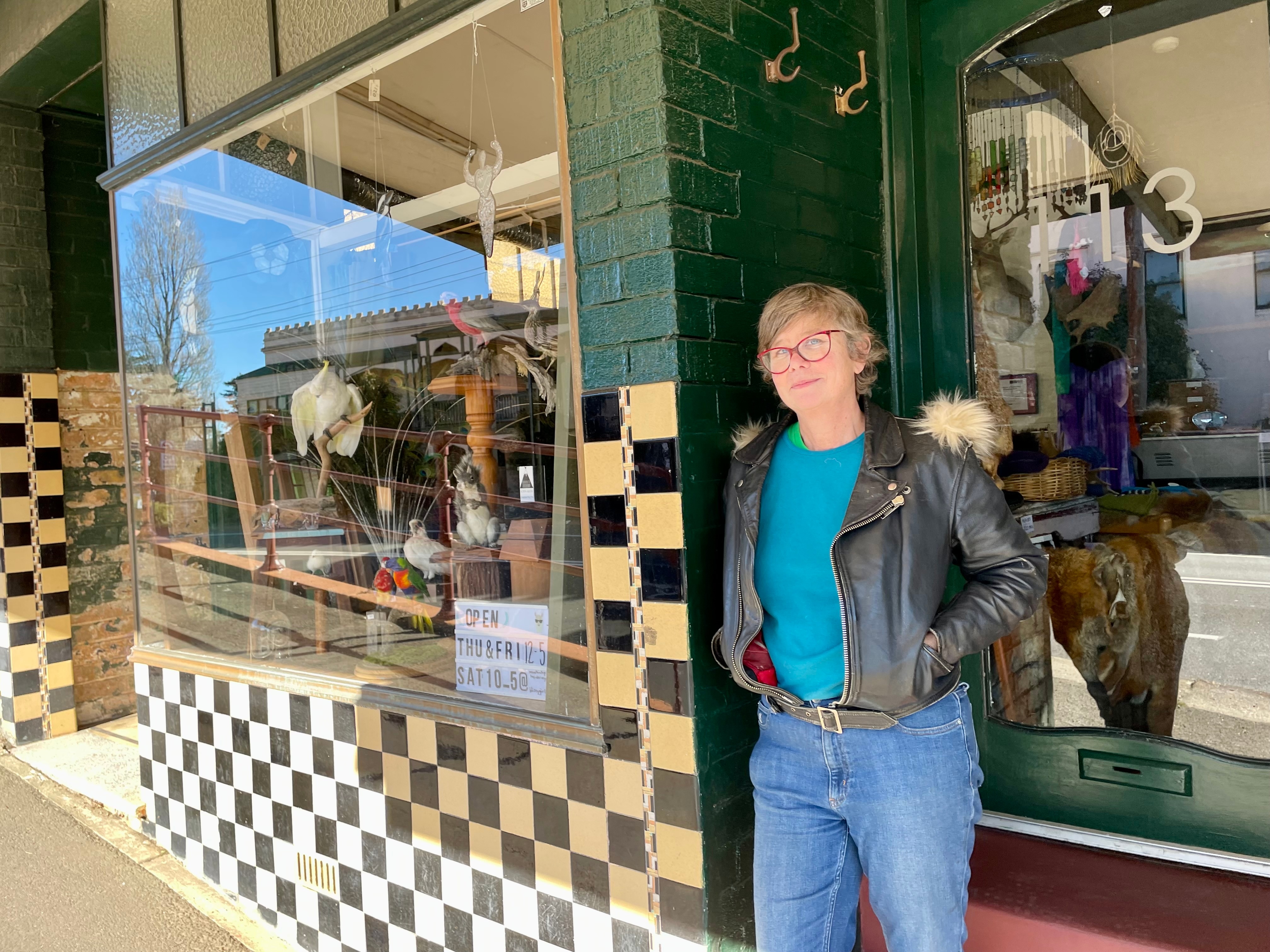 A smiling woman standing in a shop doorway with a glass window