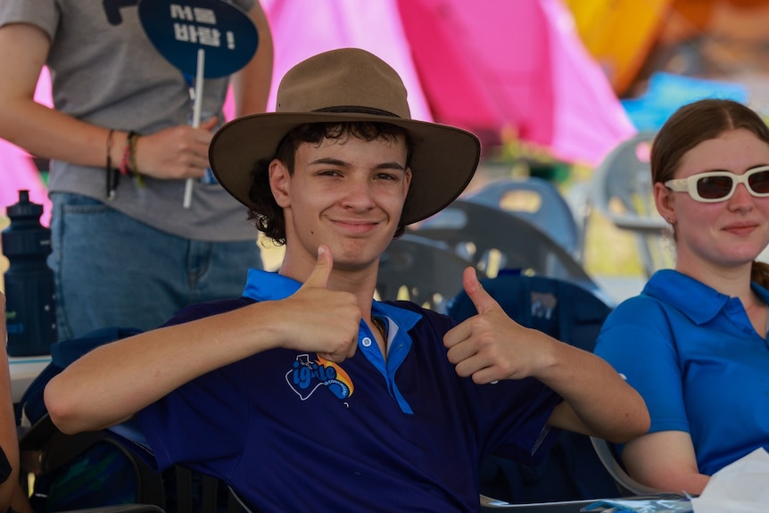 Teenage boy with clammy skin wears an Akubra hat. He gives two thumbs up and smiles