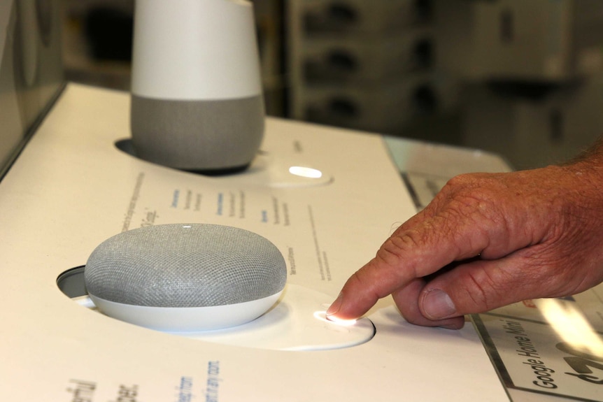 A man presses the button of a Google Home Mini device on a display stand in a shop.