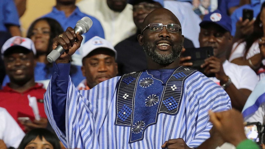 George Weah smiles while surrounded by supporters.