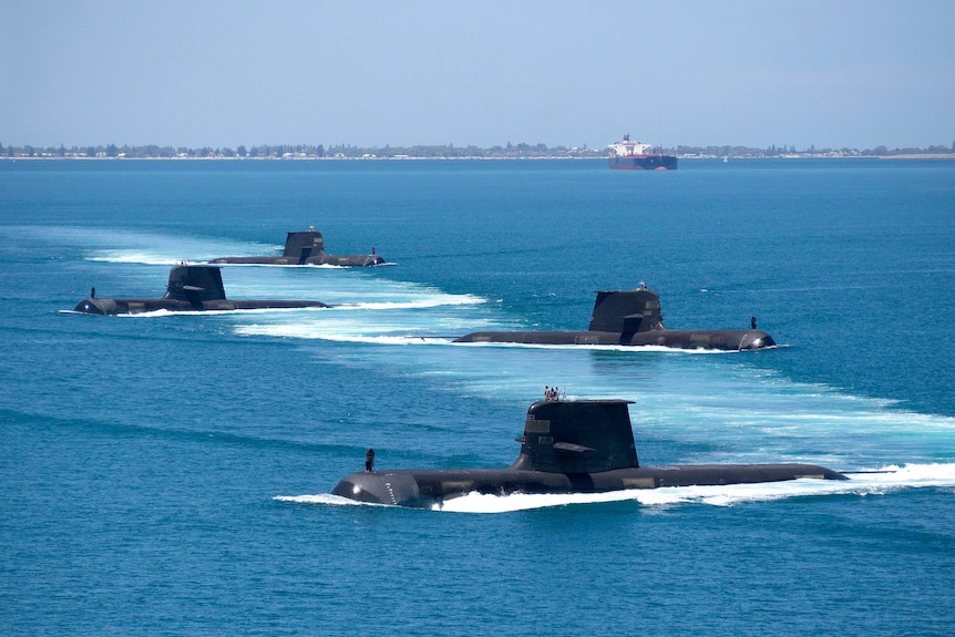 Four submarines jut out of a bright blue ocean, sailing together in formation