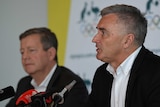 Matt Carroll and Ian Chesterman sit at a press conference wearing white open-necked shirts and black suits