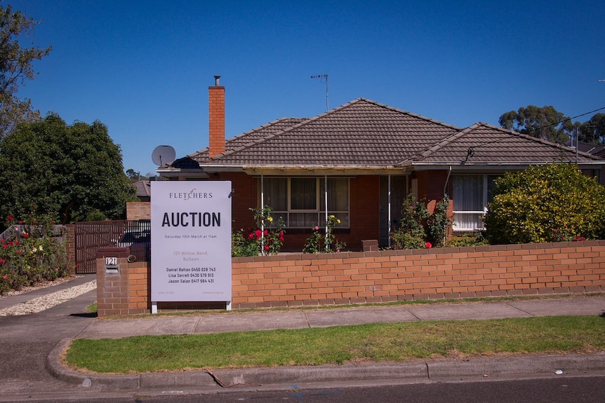A red brick home with a sign out the front saying 'auction'.