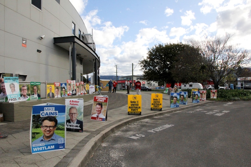 Election signs lined up outside a brick building.