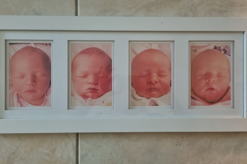An image taken of a white photo frame with a headshot portrait of four babies' faces side by side, laying on cream tiles