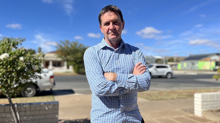 A frowning man wearing a shirt with his arms crossed in front of a street. 