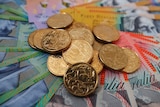 A pile of Australian one dollar coins sits on banknotes of various denominations.