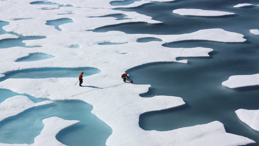 Two people are seen walking on slabs of ice in the Arctic Circle.