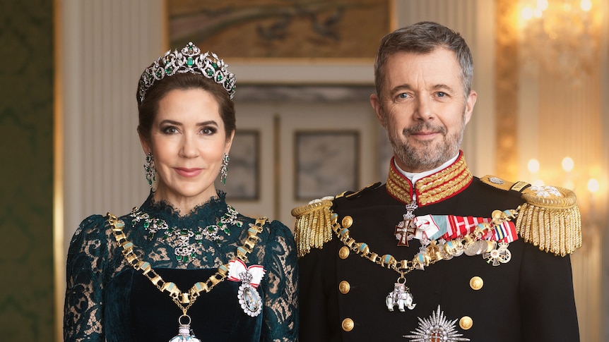 Queen Mary and King Federick of Denmark smile standing sude by side wearing royal attire.