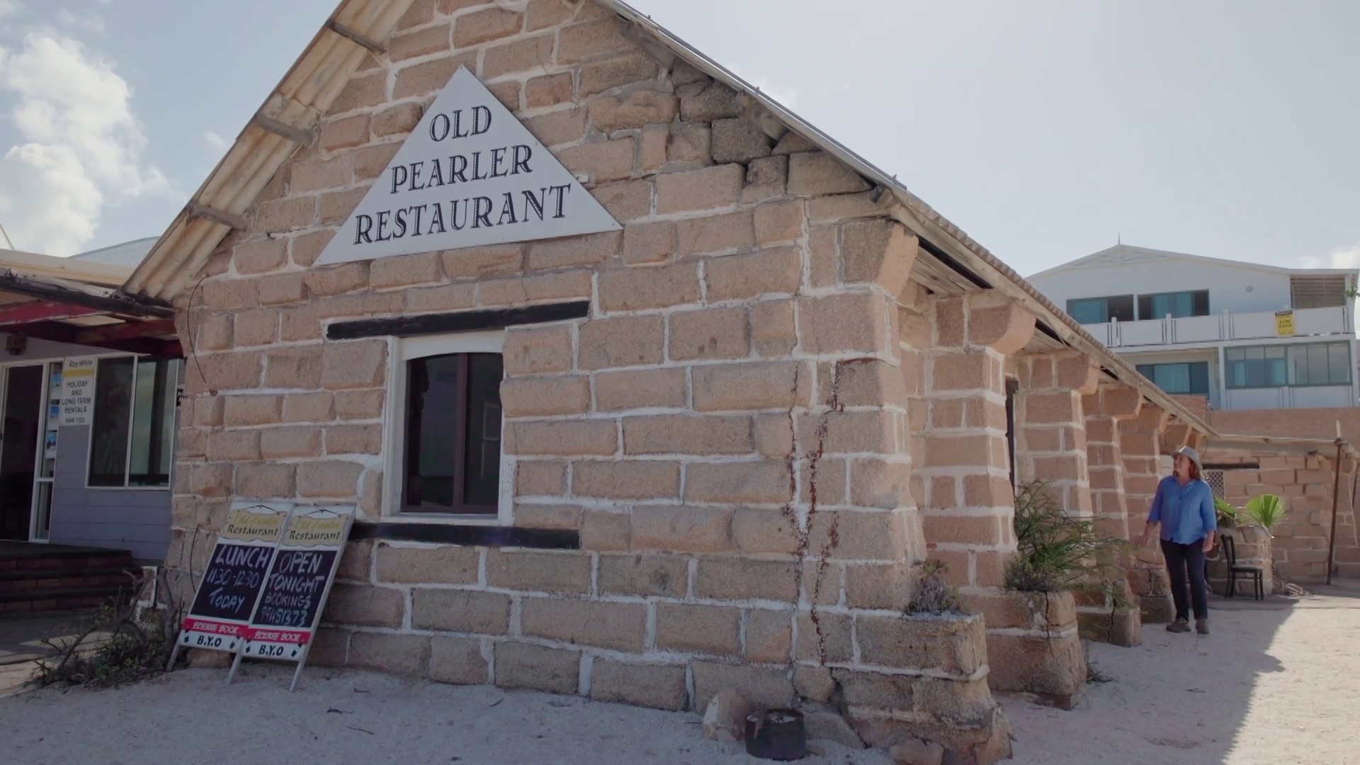 Lisa Millar se encuentra junto a un antiguo edificio llamado Pearler Restaurant.
