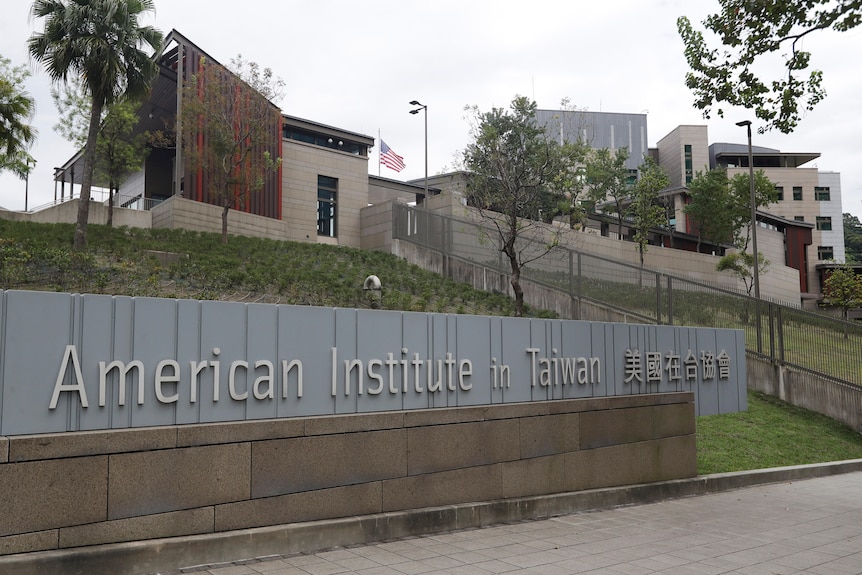 A drab but mode grey and brown secure building sits on a grassy hillside in Taiwan. The American flag is visible.