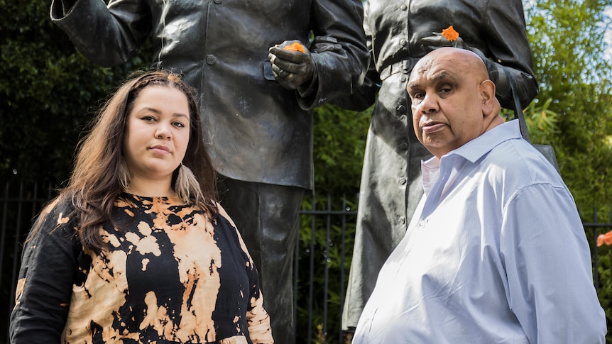 Bumpy and Kutcha Edwards stand in front of two bronze statues which are out of focus. they look towards the camera.