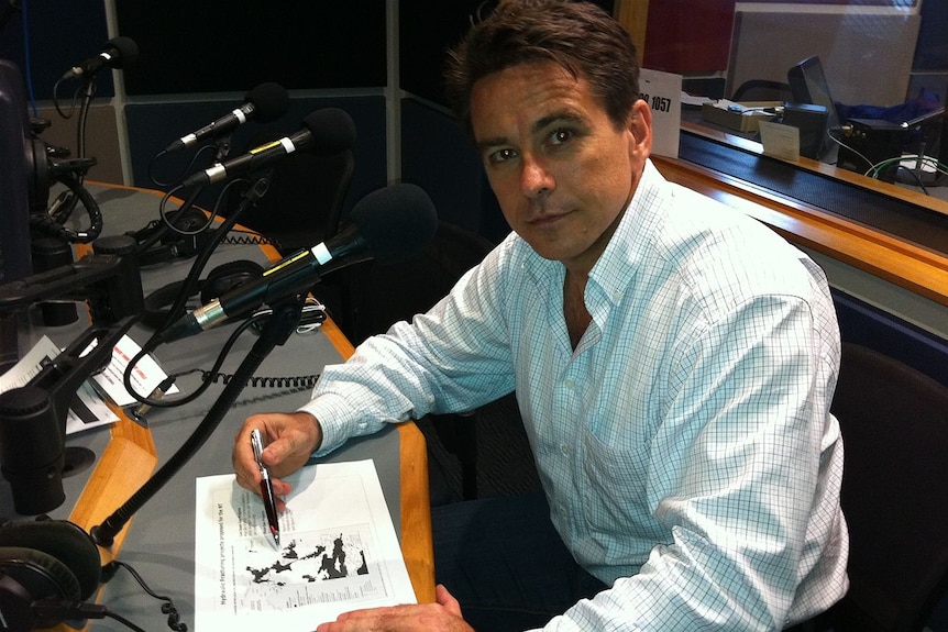 Man in a radio studio looking at camera with a a map laid before him.