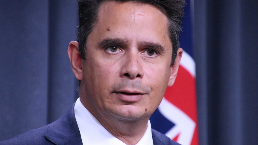 A tight head and shoulders shot of WA Treasurer Ben Wyatt in a suit and tie standing in front of an Australian flag.