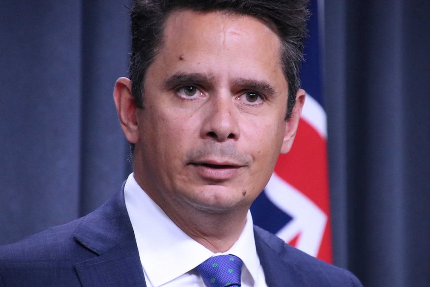 A tight head and shoulders shot of WA Treasurer Ben Wyatt in a suit and tie standing in front of an Australian flag.