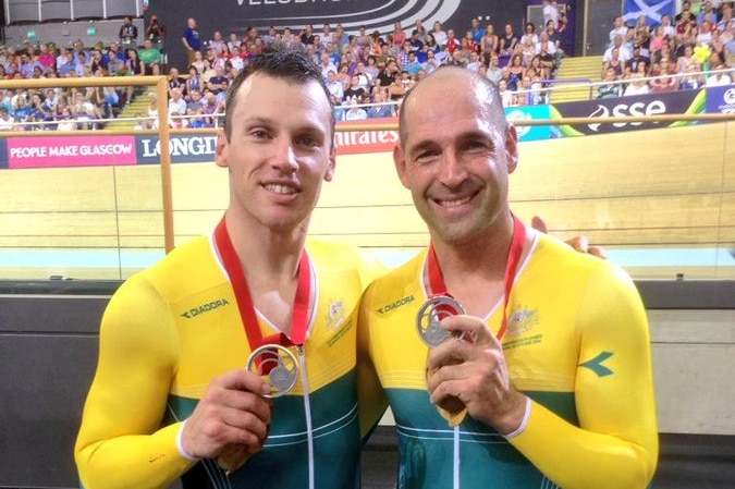 Two men standing in cycling uniforms holding up silver medals