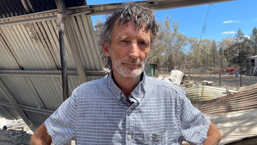 Tara resident Mark Lacy at the scene of his property after it was destroyed by fire, twisted metal, blackened metal behind him