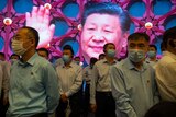 People in Covid masks walk past a screen featuring a waving Xi Jinping