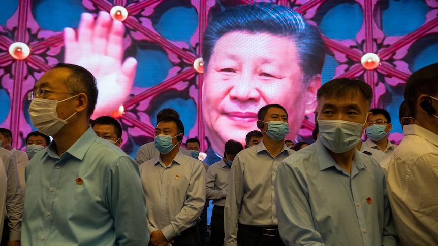 People in Covid masks walk past a screen featuring a waving Xi Jinping