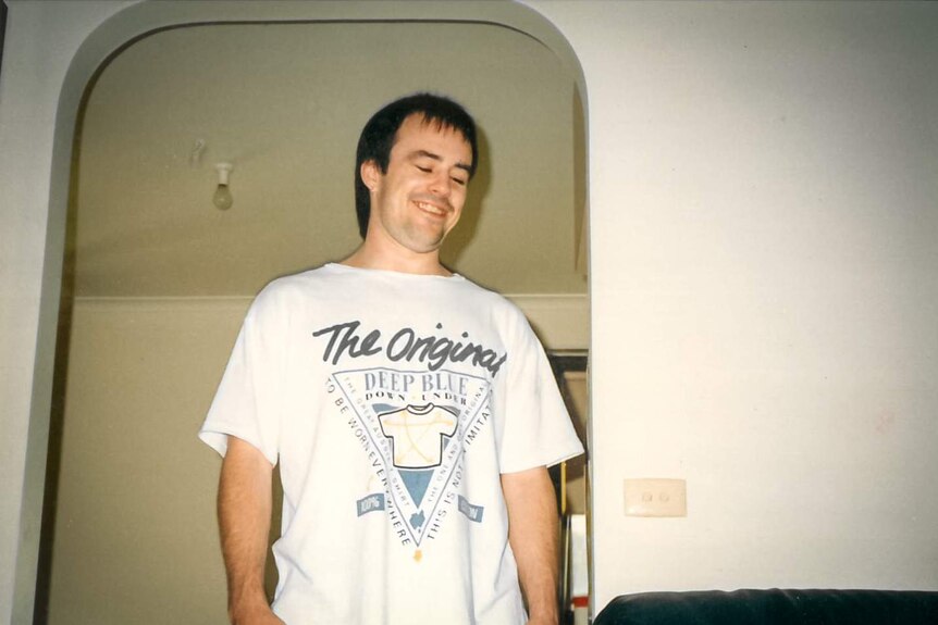 Stephen Asling wearing a white t-short inside a house, smiling in an old photograph.
