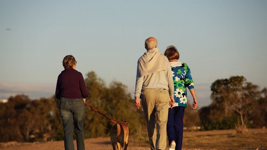 Three people walking a dog along a dirt road