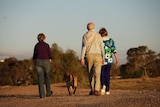 Three people walking a dog along a dirt road