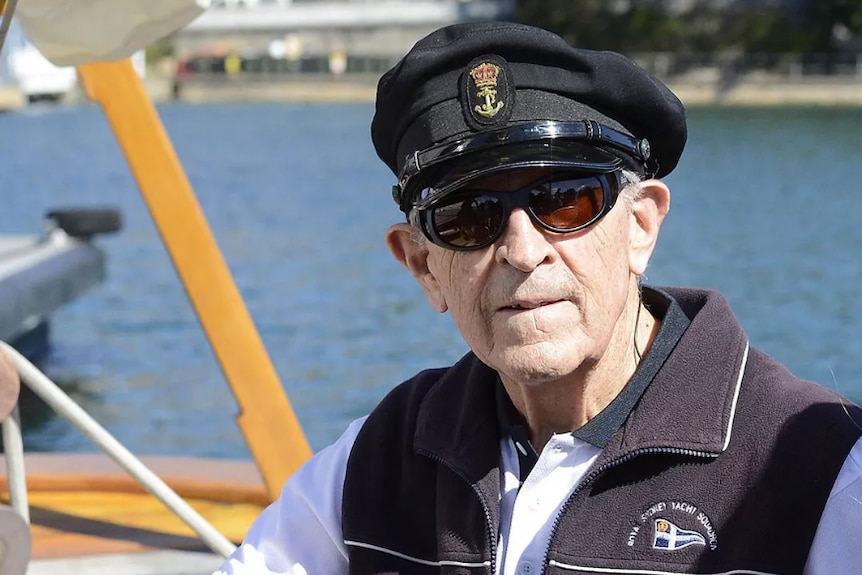 A man on a boat wearing sunglasses and a cap smiles.