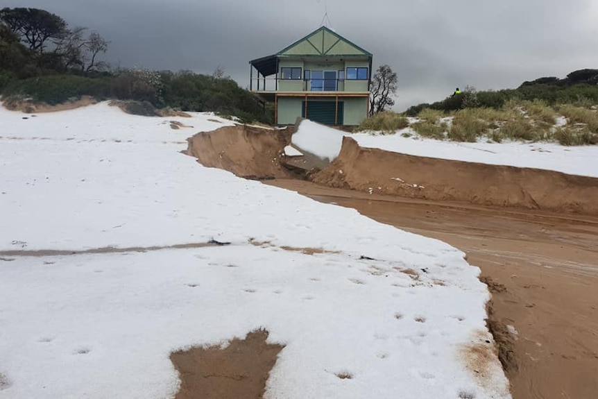 A damaged building on a beach with white hail on the sand in the foreground.