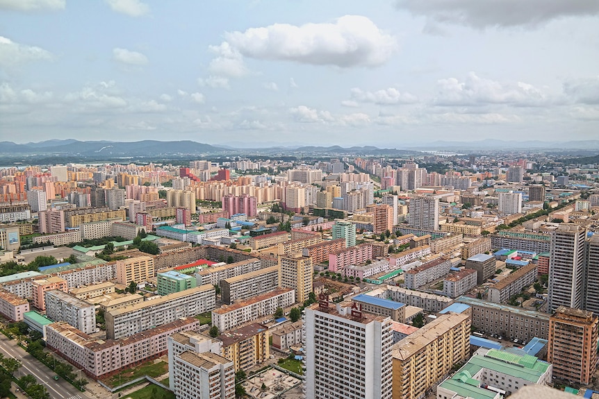 Wide colour photo of Pyongyang cityscape, Taedong river and Rungrado May Day Stadium in front of mountain terrain on a clear day