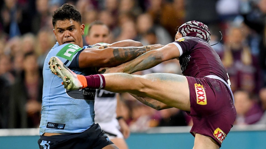 A rugby league player tries to get away while his opponent hangs on to him with his leg in the air.