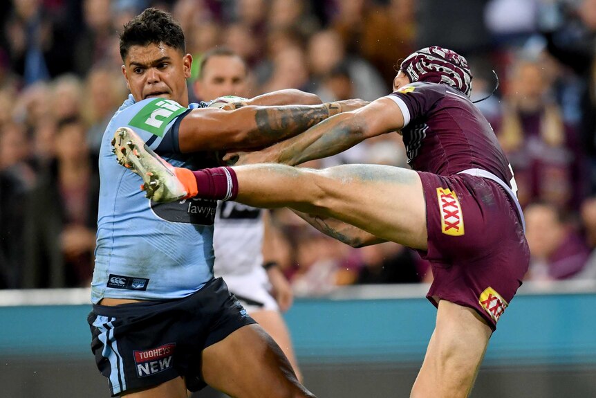 A rugby league player tries to get away while his opponent hangs on to him with his leg in the air.