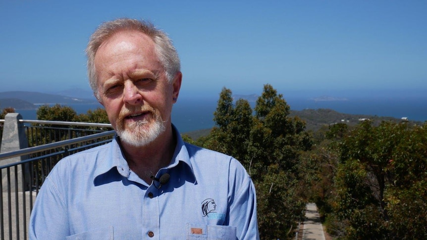 Man stands on top of mountain in Albany, with ocean and bushland in background.