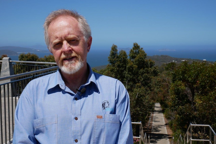 Man stands on top of mountain in Albany, with ocean and bushland in background.