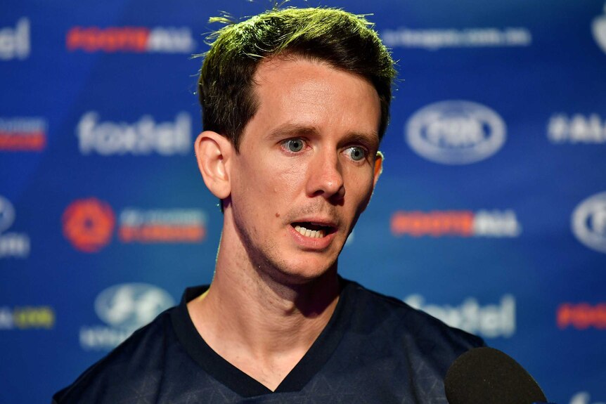 Robbie Kruse stands and talks in front of a blue backdrop
