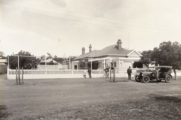 Black and white image of federation house, tennis court, people on street outside with 1920s motor car.