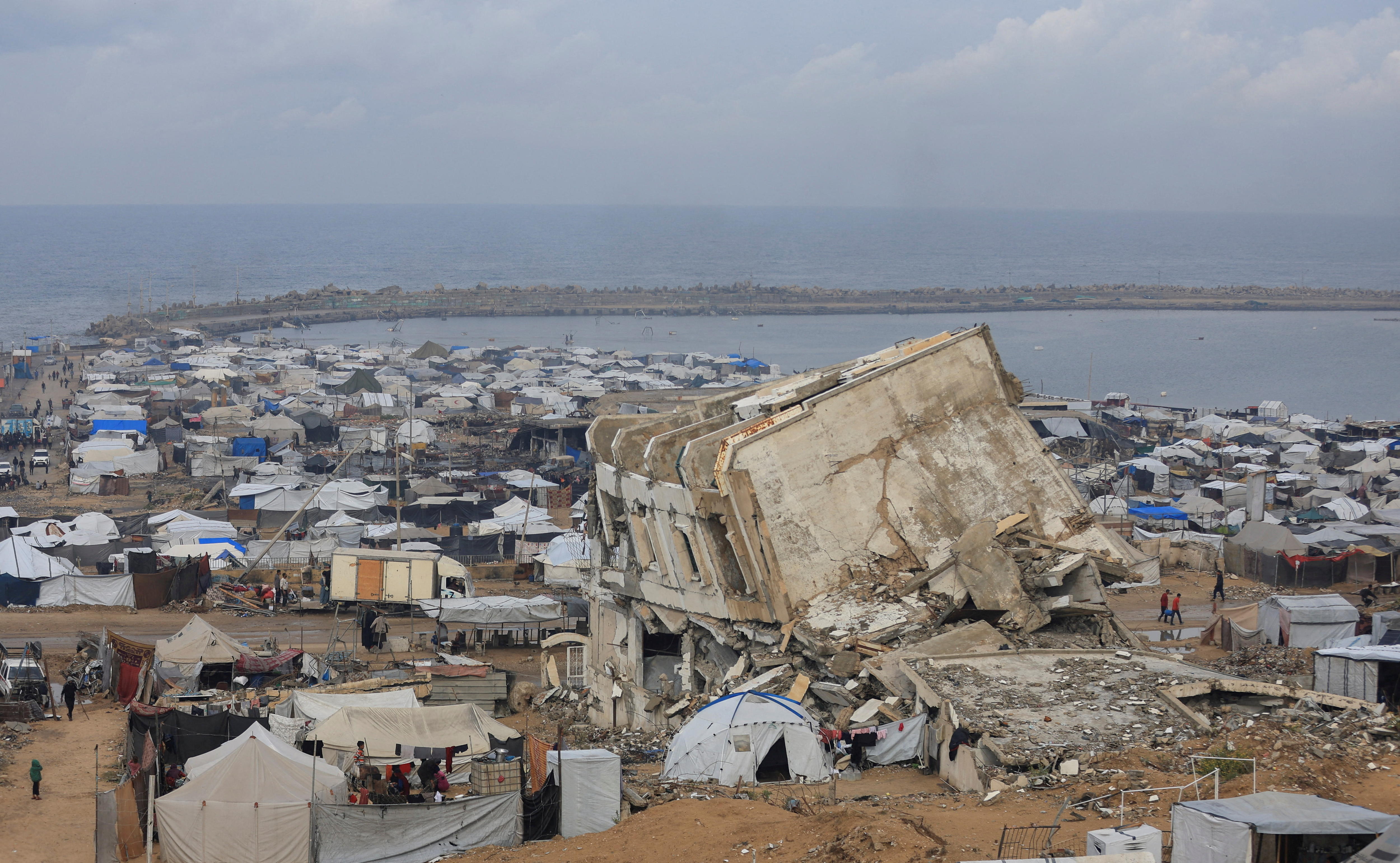 Makeshift tents crowd a coastline amid rubble.