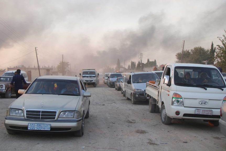 Cars are seen in a long line as thick smoke raises in the background.