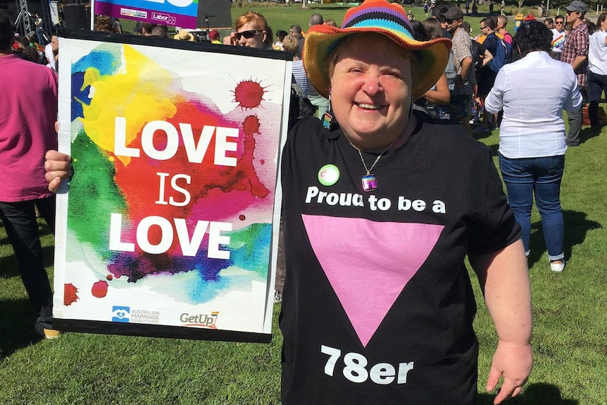 Meredith wears a shirt saying "proud to be a 78er" and holds a love is love sign.