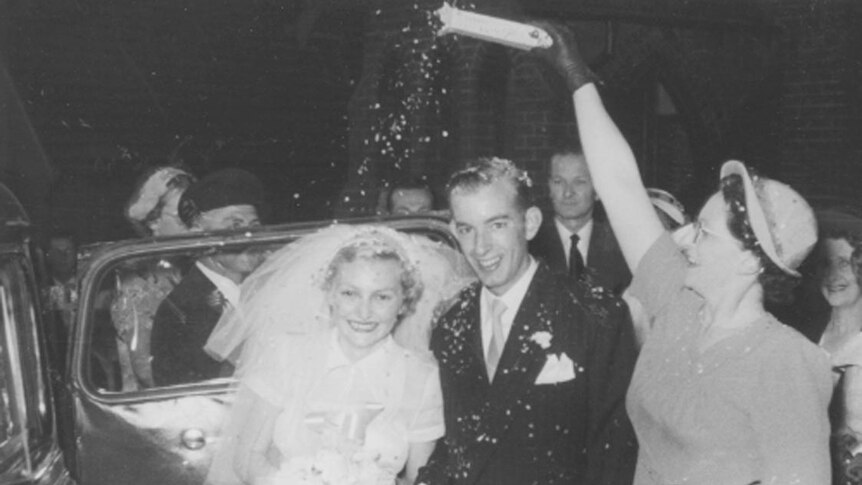 A black and white photograph of a young newly married couple smiling, being scattered with rice.