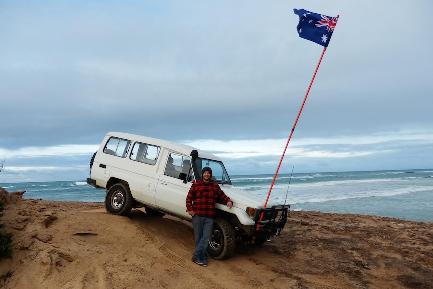 Made poses with a 4WD vehicle with Aussie flag on sand at a beach