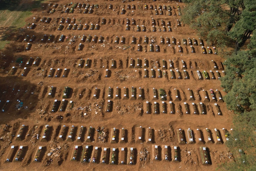 An aerial shot showing scores of mass graves in red-brown dirt from above.