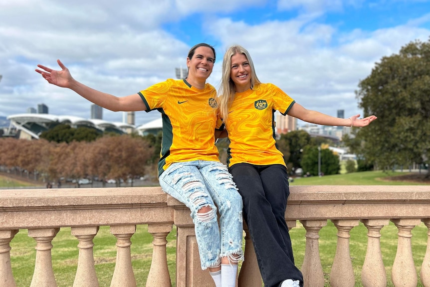 Matildas players Lydia Williams and Charli Grant link arms.