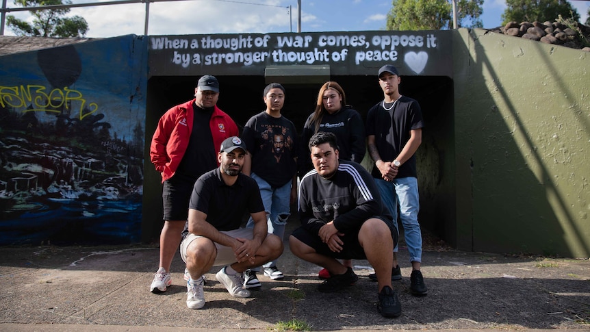 Members of Manifold standing in front of overpass walkway, which has a Baha'i quote about peace painted on it.