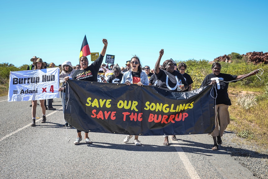 A group of people holding signs as they march on a road, protesting against industry development.