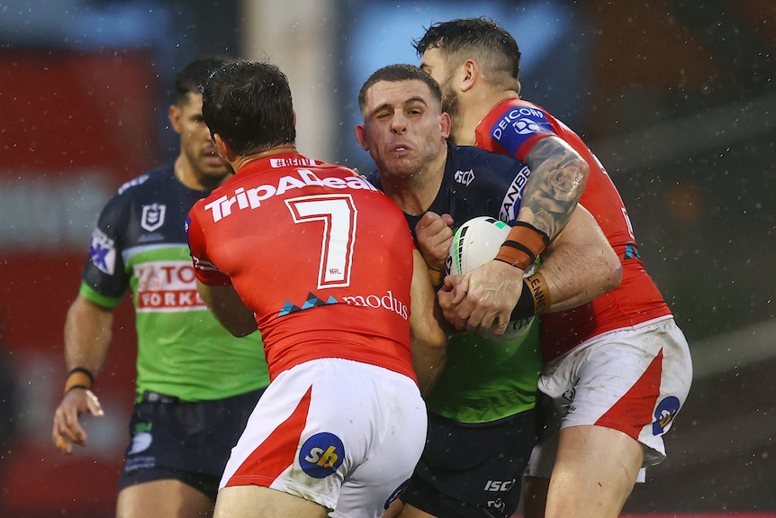 A Canberra Raiders NRL player is tackled by two St George Illawarra opponents.
