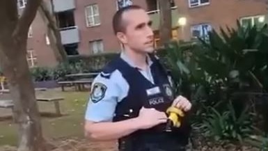 A male police officer stands in front of an apartment block