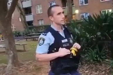 A male police officer stands in front of an apartment block