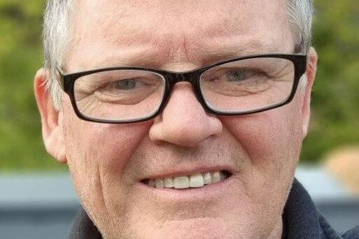 A man with short grey hair and glasses, smiling.